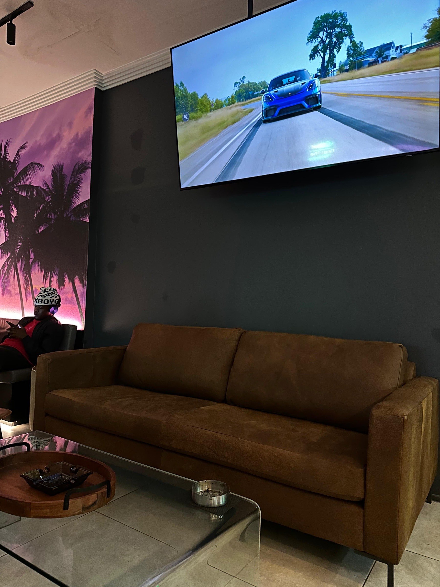 Cognac leather sofa, sunset palm mural, driving game on the wall TV.